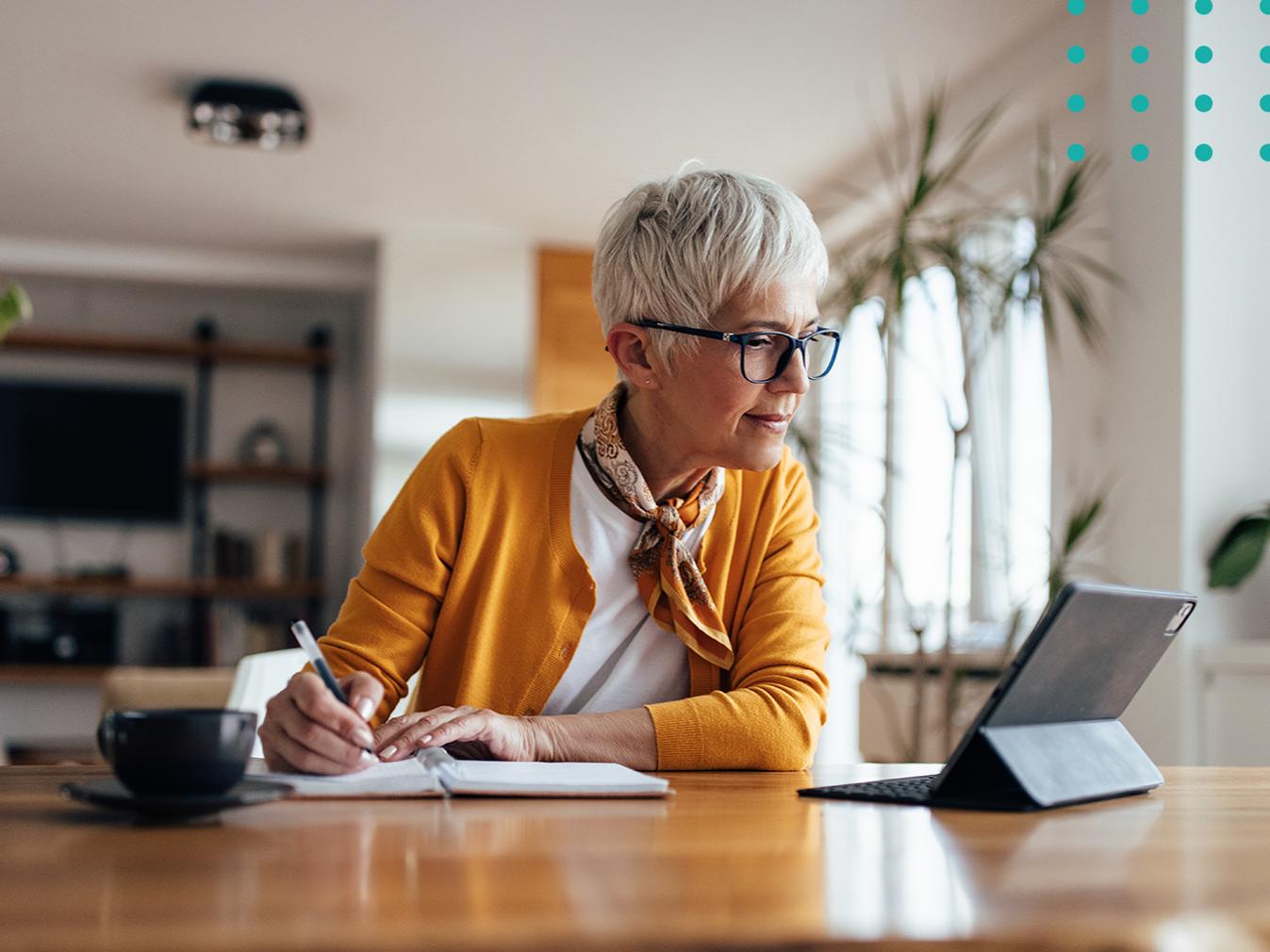 woman taking notes on a notepad while looking at a tablet